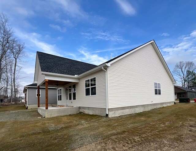 view of side of home with a patio, roof with shingles, and a lawn