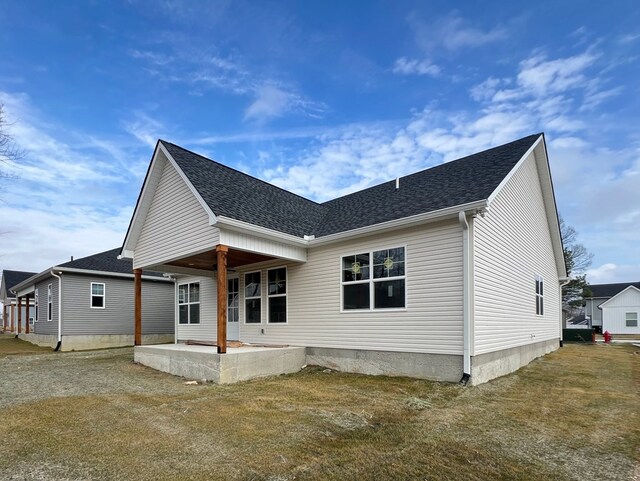 back of house with a shingled roof, a patio area, and a lawn