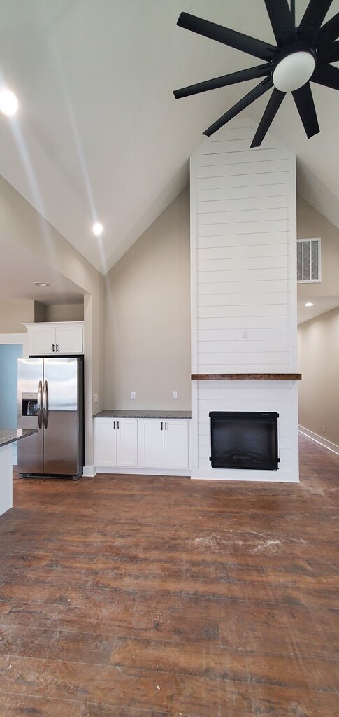 unfurnished living room featuring ceiling fan, a large fireplace, dark wood-style flooring, visible vents, and baseboards