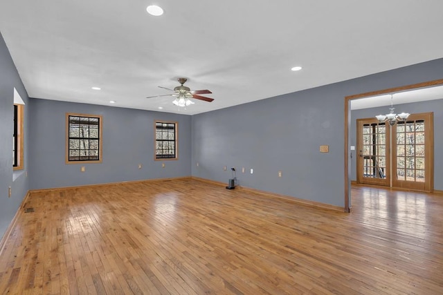 unfurnished room with ceiling fan with notable chandelier, light wood finished floors, baseboards, and a healthy amount of sunlight