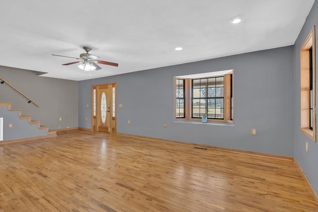 empty room with ceiling fan, visible vents, baseboards, stairway, and light wood-type flooring