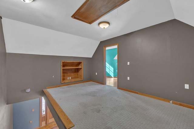 bonus room featuring built in shelves, carpet, attic access, vaulted ceiling, and baseboards