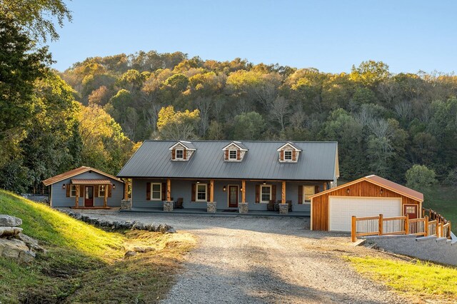 view of front of house featuring a view of trees, a detached garage, metal roof, covered porch, and an outdoor structure