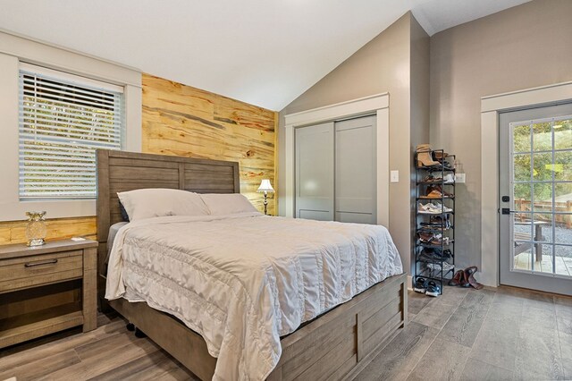 bedroom with access to outside, vaulted ceiling, wood walls, and wood finished floors