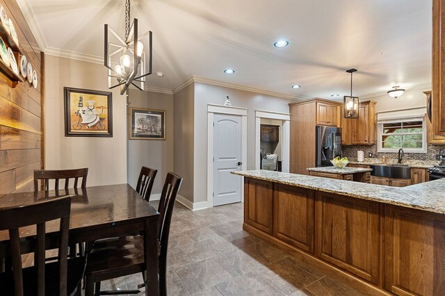 kitchen with stainless steel fridge, brown cabinets, decorative light fixtures, light stone countertops, and a sink