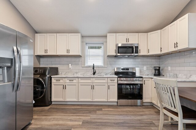 kitchen featuring white cabinets, light stone counters, appliances with stainless steel finishes, washer / clothes dryer, and a sink