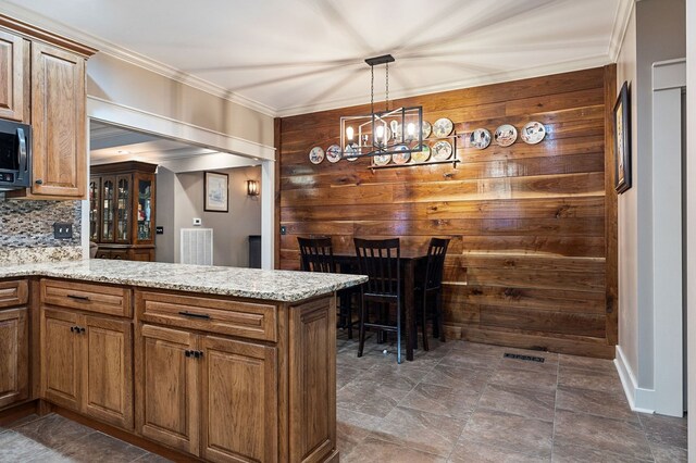 kitchen featuring tasteful backsplash, ornamental molding, brown cabinets, a peninsula, and light stone countertops