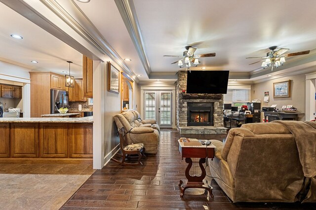 living area featuring a ceiling fan, a tray ceiling, a fireplace, and ornamental molding