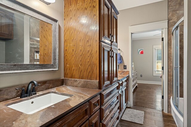 bathroom with shower / bath combination with glass door, wood finished floors, vanity, baseboards, and crown molding