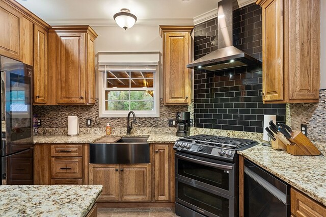 kitchen with tasteful backsplash, light stone counters, wall chimney range hood, double oven range, and a sink