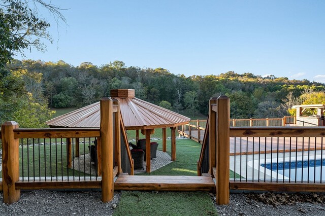 deck with a forest view, a gazebo, a fenced in pool, and a yard