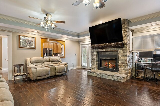 living area with ceiling fan, a stone fireplace, ornamental molding, and dark wood finished floors