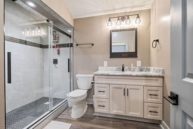 bathroom with a textured ceiling, toilet, wood finished floors, vanity, and a shower stall