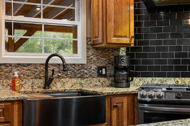 kitchen with light stone countertops, gas range, brown cabinetry, and a sink