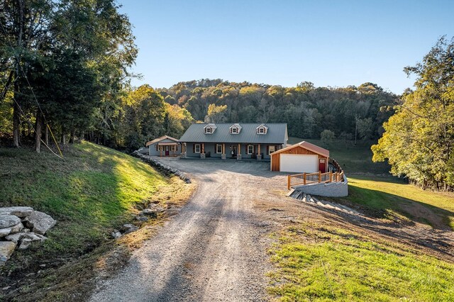 view of front of home featuring a front yard, metal roof, a garage, driveway, and a forest view