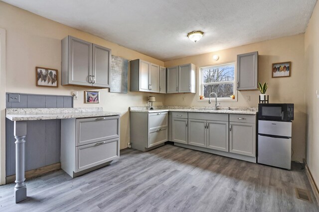 kitchen with gray cabinetry, freestanding refrigerator, a sink, wood finished floors, and black microwave