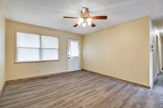 empty room featuring a ceiling fan, baseboards, visible vents, and wood finished floors