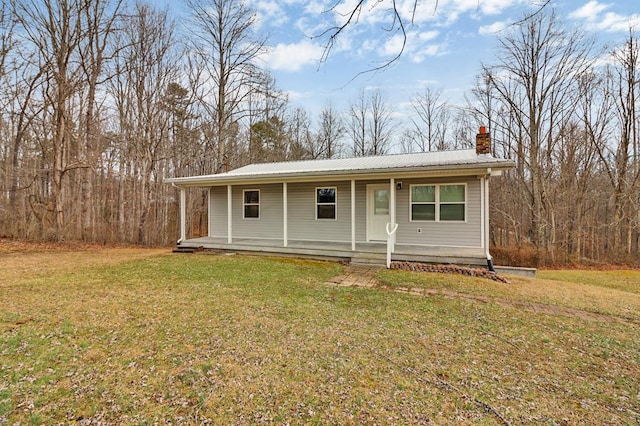 view of front of property featuring covered porch, metal roof, a chimney, and a front lawn