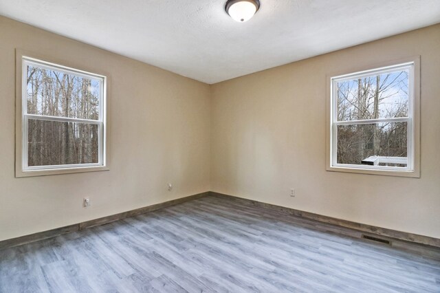 empty room featuring baseboards, wood finished floors, visible vents, and a healthy amount of sunlight