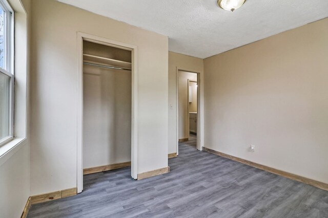 unfurnished bedroom with a closet, a textured ceiling, baseboards, and wood finished floors