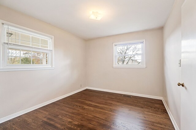 spare room featuring dark wood-style floors, plenty of natural light, visible vents, and baseboards