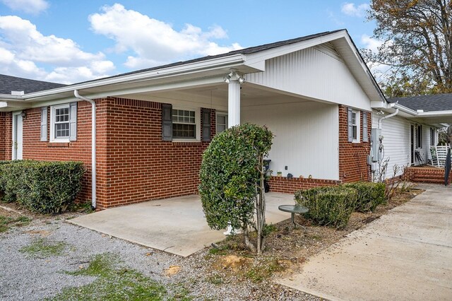 view of side of home featuring driveway, a patio, and brick siding