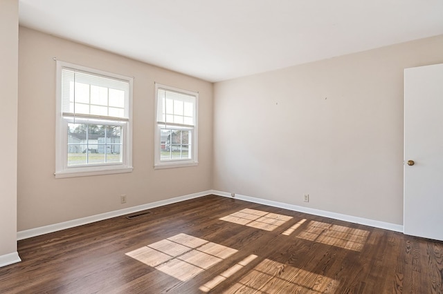 unfurnished room with dark wood-style flooring, visible vents, and baseboards