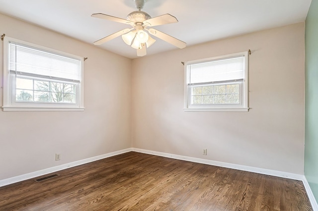 empty room with a wealth of natural light, wood finished floors, visible vents, and baseboards