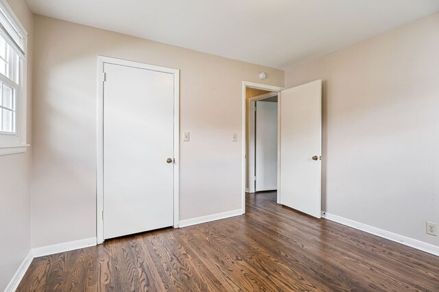 unfurnished bedroom with dark wood-style flooring and baseboards