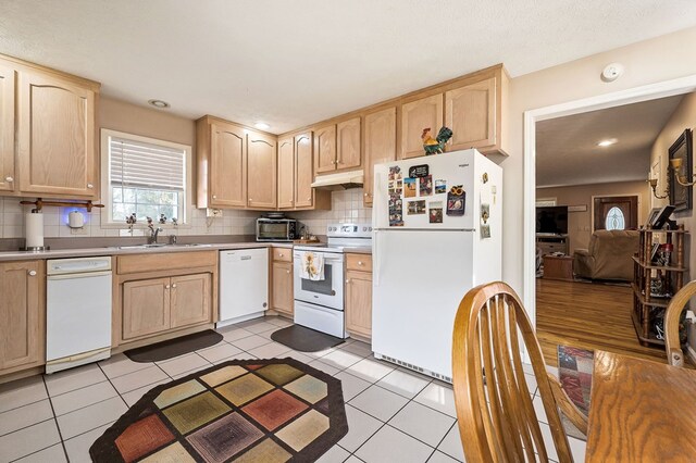 kitchen featuring light brown cabinetry, white appliances, a sink, and under cabinet range hood