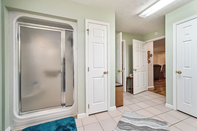 bathroom featuring a textured ceiling, a stall shower, tile patterned flooring, and baseboards