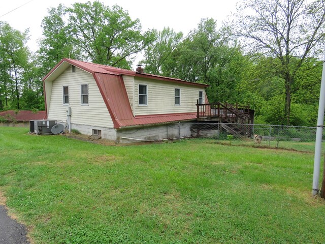 rear view of property featuring a lawn, a gambrel roof, metal roof, fence, and central air condition unit