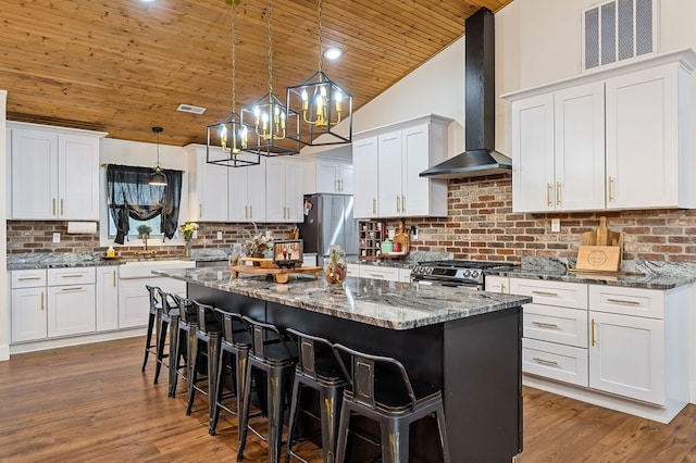 kitchen with wall chimney exhaust hood, appliances with stainless steel finishes, decorative light fixtures, and white cabinets