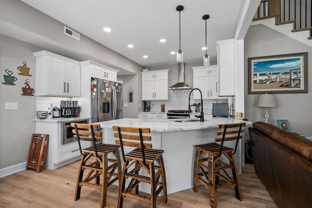 kitchen with a peninsula, a sink, wall chimney range hood, appliances with stainless steel finishes, and light wood finished floors