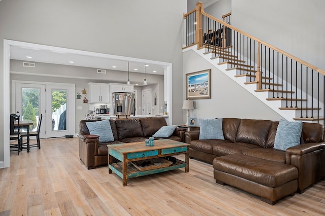 living room with light wood-style flooring, stairway, a towering ceiling, and visible vents