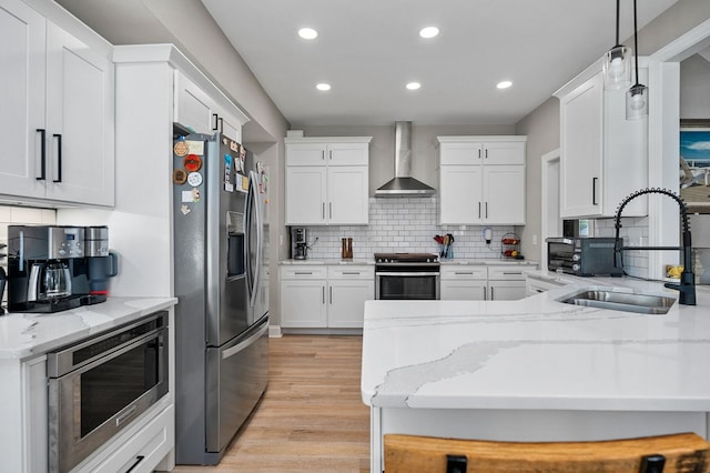 kitchen featuring stainless steel appliances, white cabinetry, a sink, and wall chimney exhaust hood