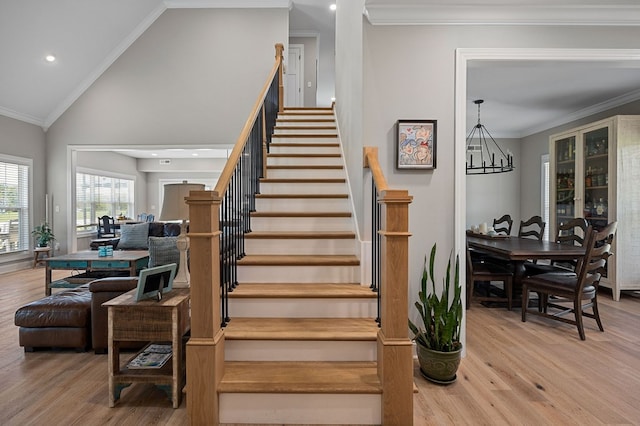 stairs with high vaulted ceiling, ornamental molding, wood finished floors, and a notable chandelier