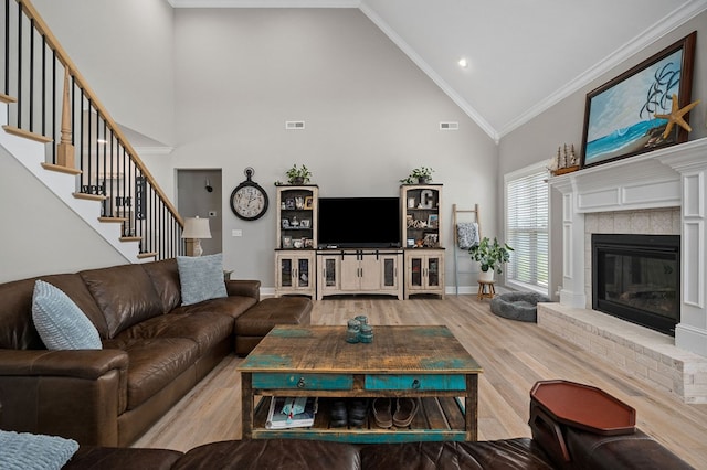 living area with ornamental molding, a brick fireplace, wood finished floors, baseboards, and stairs