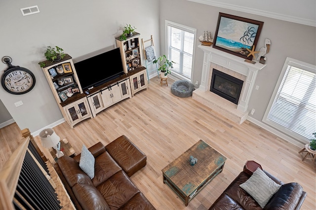 living area featuring wood finished floors, visible vents, baseboards, ornamental molding, and a glass covered fireplace