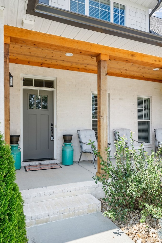 doorway to property featuring a porch and brick siding