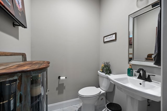 half bathroom featuring toilet, marble finish floor, baseboards, and a sink