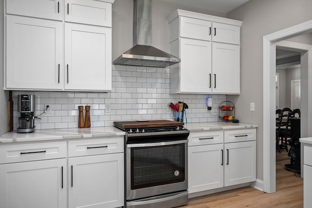 kitchen featuring tasteful backsplash, electric stove, wall chimney exhaust hood, light wood-type flooring, and white cabinetry