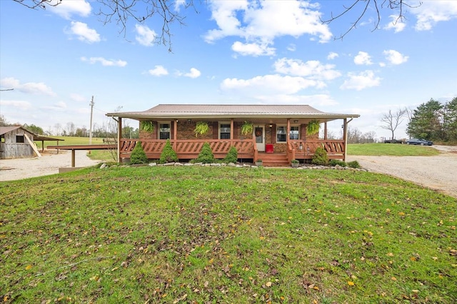 view of front of home featuring dirt driveway, metal roof, covered porch, and a front yard