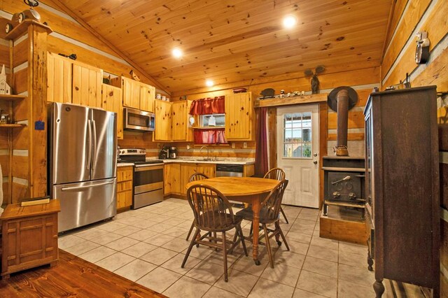 kitchen featuring stainless steel appliances, a sink, vaulted ceiling, light countertops, and a wood stove