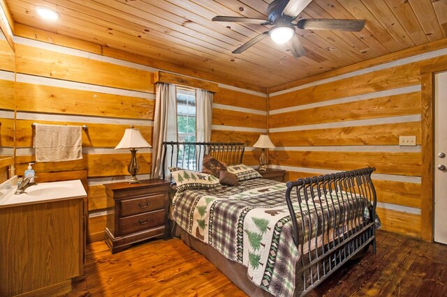 bedroom with dark wood-style floors, wood ceiling, a sink, and wood walls