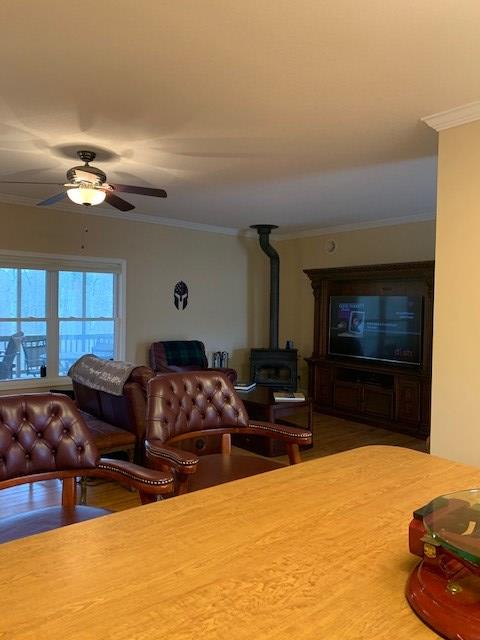 living room with a wood stove, ceiling fan, and crown molding