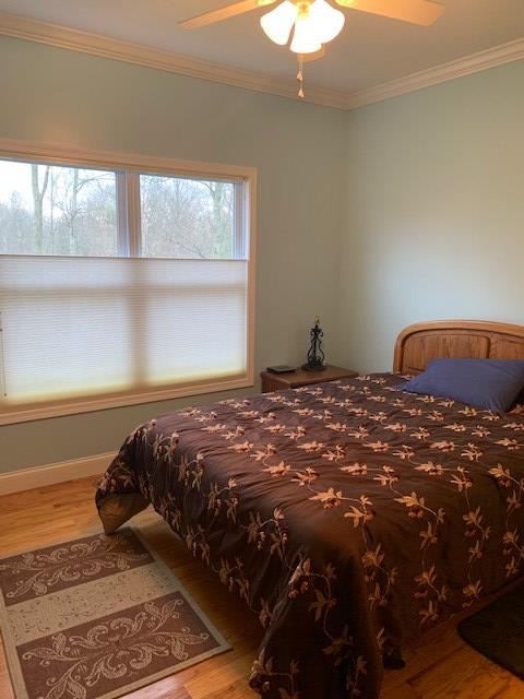 bedroom with ceiling fan, crown molding, baseboards, and wood finished floors