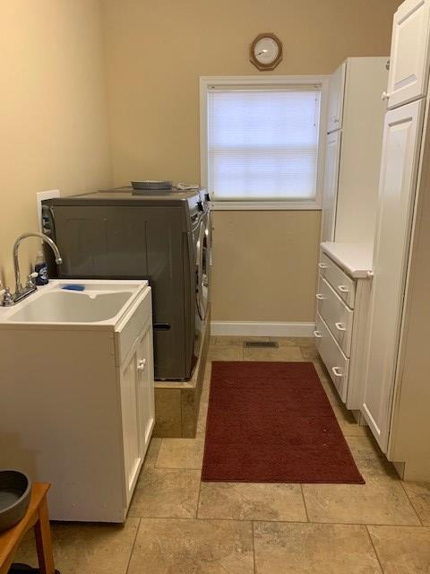 washroom featuring cabinet space, washing machine and dryer, baseboards, and a sink