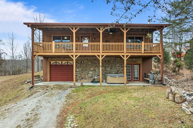 view of front facade with central air condition unit, a hot tub, an attached garage, stone siding, and driveway