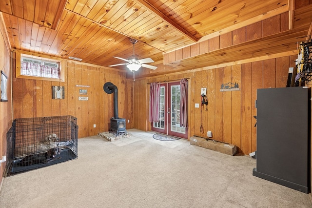 unfurnished living room featuring a wealth of natural light, wooden ceiling, a wood stove, and light colored carpet